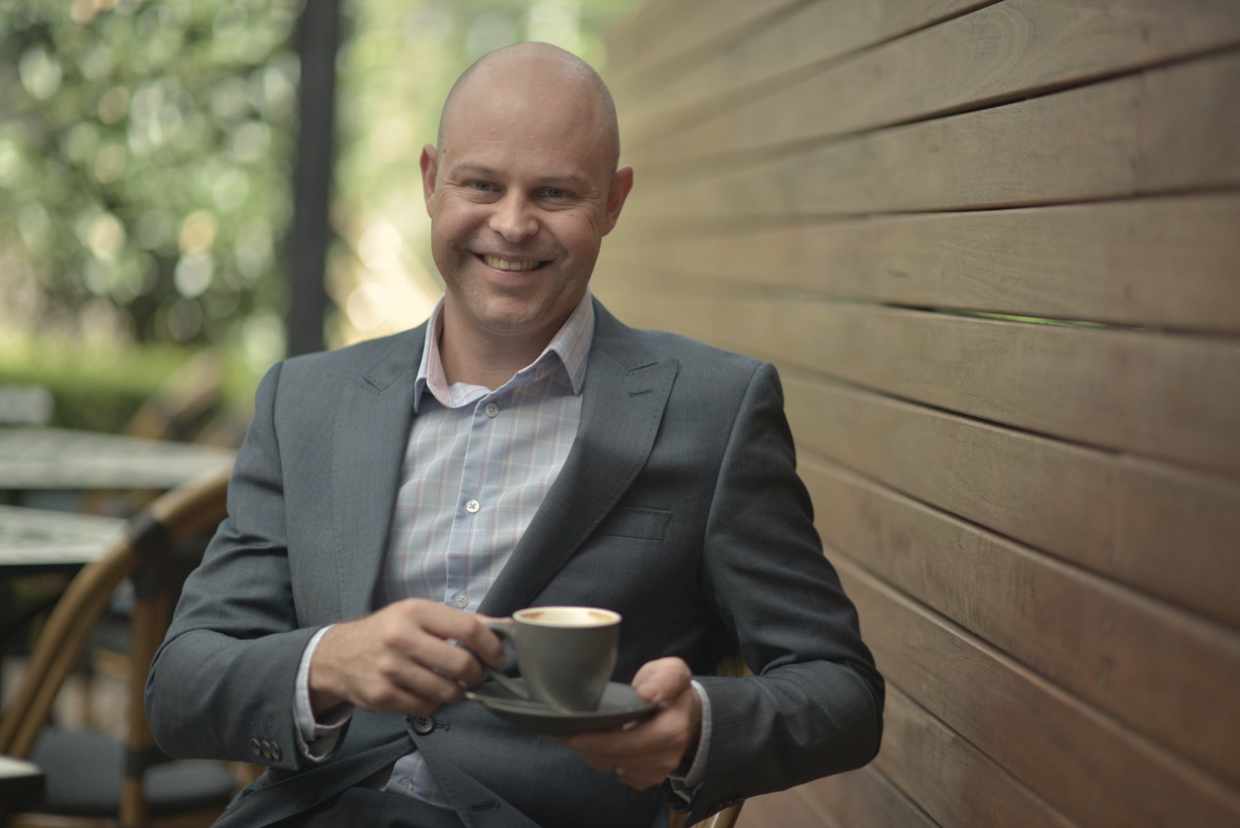 Joe Combrink smiling, holding a cup of coffee at an outdoor café
